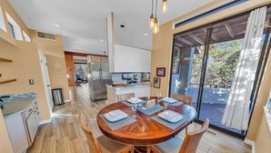 A modern kitchen with white cabinets and stainless steel appliances, a dining area with a wooden table and chairs, and a large sliding glass door leading to an outdoor deck.