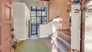 A modern interior with a wooden staircase, a green rug, and a view through a glass door.
