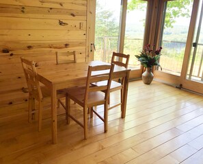 Ein Holzespeisetisch mit vier Stühlen, einer Topfpflanze und Blick auf einen Wald durch große Fenster.