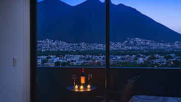 Quarto com vista para um horizonte urbano e montanhas ao entardecer.