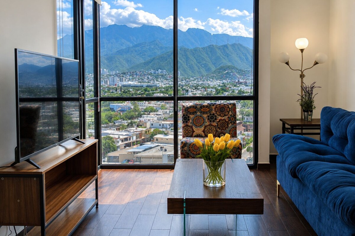 A modern living room with a large window, a flat-screen TV, a sofa, a coffee table with a vase of flowers, and a lamp.