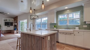 A modern kitchen with a central island, white cabinetry, and a large window providing natural light. - Outdoor Living Area * A/C * Custom Built Home (Encinitas)