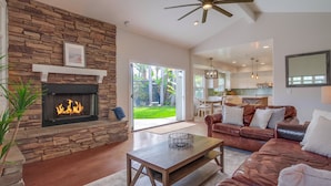 A spacious living room with a stone fireplace, leather sofa, and a view into the kitchen and backyard. - Outdoor Living Area * A/C * Custom Built Home (Encinitas)