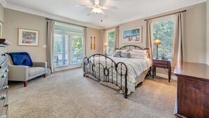 Een slaapkamer met een bed, een plafondventilator, een kaptafel, een stoel en een raam met gordijnen.