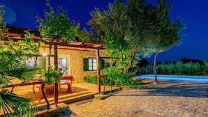 A stone building with a wooden pergola, a bench, and a pool area.