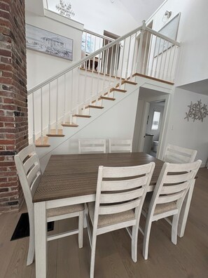 Ein Essbereich mit Holztisch, weißen Stühlen, einer Backstein-Säule und einer Treppe mit weißen Geländern.