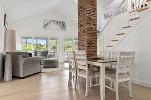 A spacious living room with a grey sofa, a dining table with white chairs, and a brick fireplace. - Cozy, open-concept, Parker River House. Waterfront, boat slip, pet-friendly! (Newbury)