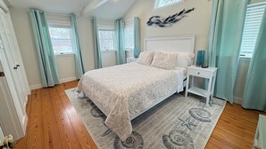 Un dormitorio con una cama grande, una mesita de noche, un aparador y una ventana con cortinas.