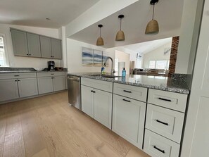 Eine moderne Küche mit weißen Schränken, Granit Arbeitsplatten und einem Geschirrspüler. Über der Spüle hängen drei Pendelleuchten.