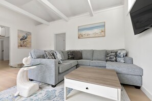 A modern living room with a grey sectional sofa, a glass coffee table, and a flat-screen TV mounted on the wall.