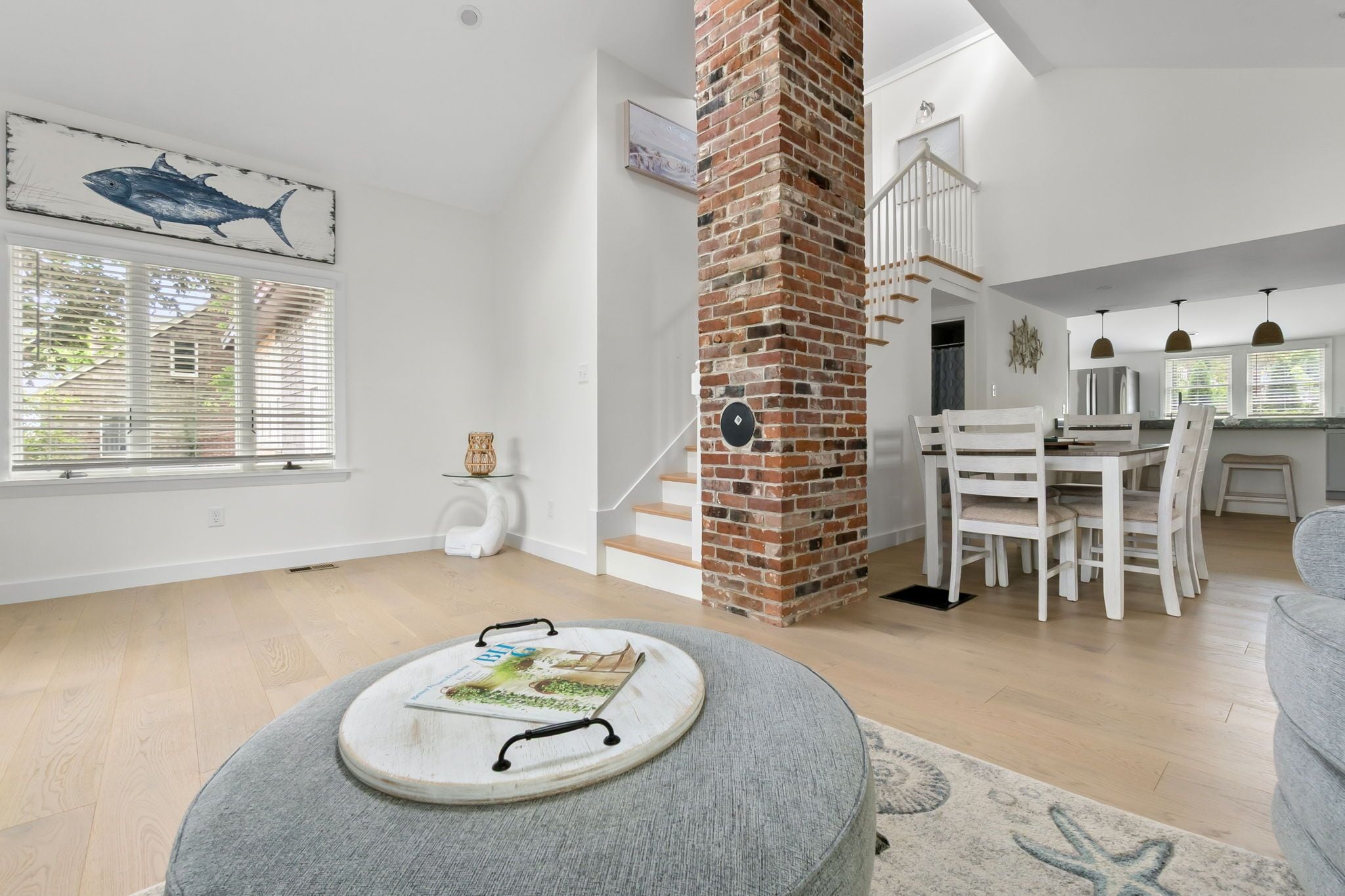 A spacious living area with a brick fireplace, a dining set, and a large window with blinds.