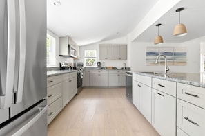 A modern kitchen with white cabinetry, a stainless steel refrigerator, and a granite countertop. - Cozy, open-concept, Parker River House. Waterfront, boat slip, pet-friendly! (Newbury)