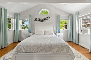 Un dormitorio con una cama grande, dos mesitas de noche, un elemento decorativo en la pared y una ventana con cortinas.