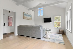 A modern living room with a grey sofa, a flat-screen TV, and a patterned rug. - Cozy, open-concept, Parker River House. Waterfront, boat slip, pet-friendly! (Newbury)