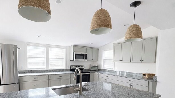 Una cocina moderna con encimeras de granito, electrodomésticos de acero inoxidable e iluminación colgante.