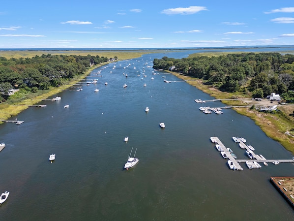 A marina with numerous boats docked along a river, surrounded by lush greenery. - Cozy, open-concept, Parker River House. Waterfront, boat slip, pet-friendly! (Newbury)