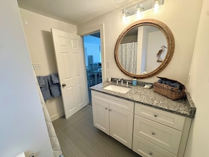 A bathroom with a granite countertop, a wooden-framed mirror, and a white door leading to a dining area. - Cozy, open-concept, Parker River House. Waterfront, boat slip, pet-friendly! (Newbury)