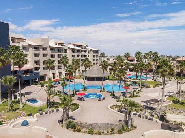 Een resort met meerdere zwembaden, palmbomen en een groot gebouw met balkons.