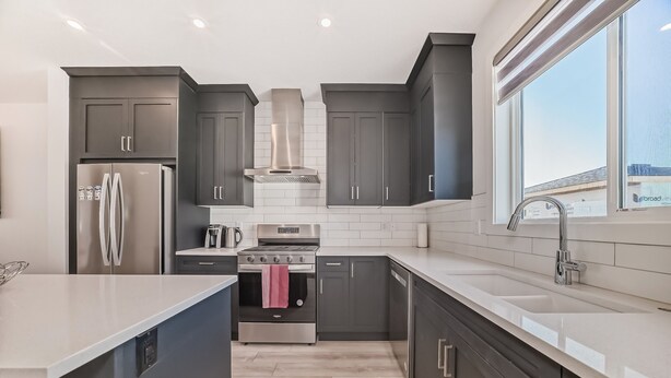 A modern kitchen with dark cabinets, stainless steel appliances, and a large window providing a view of the outside. - A Family Relaxing Vacation House, 3 bedrooms2.5 bathrooms for up to 8 people (Calgary)