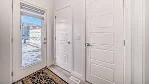 A hallway with three white doors, a patterned rug, and a view of a snowy outdoor area. - A Family Relaxing Vacation House, 3 bedrooms2.5 bathrooms for up to 8 people (Calgary)