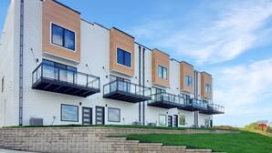 Un edificio residenziale moderno a più piani con balconi, fondamenta in mattoni e un'area verde davanti.