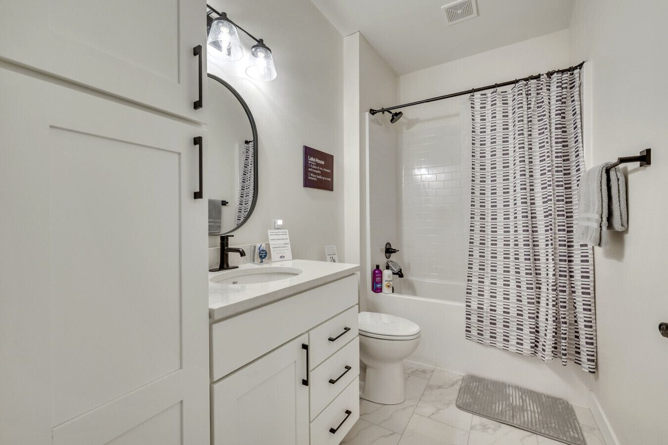 A bathroom with a white sink, mirror, and toilet. There is a shower curtain with a pattern, and a towel rack with a towel.