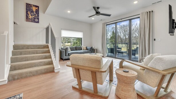 Ein geräumiger Wohnbereich mit Treppe, einem Sofa, zwei Schaukelstühlen und einer großen Glasschiebetür, die zu einer Außenpatio führt.