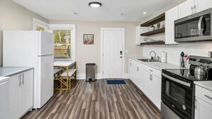 Una cucina moderna con mobili bianchi, un frigorifero in acciaio inossidabile, un forno a microonde e un piano cottura.