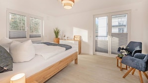 Une chambre à coucher avec un lit, une table de chevet, une lampe, une chaise, une plante en pot et une vue par la fenêtre.