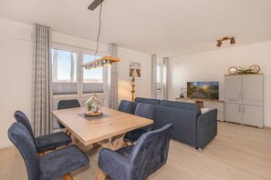 Un salon moderne avec une table à manger en bois, des chaises bleues, un canapé gris, un téléviseur et un meuble.