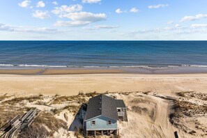 Una casa frente a la playa, con arena y vista al océano.