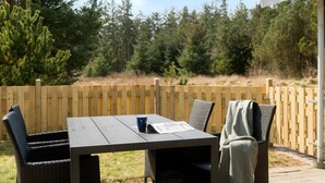 An outdoor patio with a table and chairs, a wooden fence, and a forested background. - Cozy home in Nørre Nebel with sauna (Nørre Nebel)