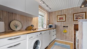 A compact kitchen with wooden paneling, white cabinetry, a Siemens washing machine, a microwave, and a sink. - Cozy home in Nørre Nebel with sauna (Nørre Nebel)
