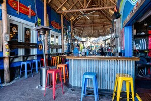 A bar area with stools, a bar counter, and a thatched roof.