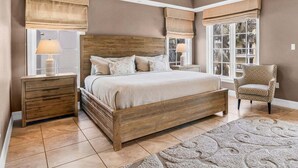 A bedroom with a wooden bed, bedside tables, a chair, and large windows with curtains. - Oasis at Beach Villas | Walk to Siesta Key Beach, Multiple Balconies, Semi-Private Pool and Spa (Sarasota)