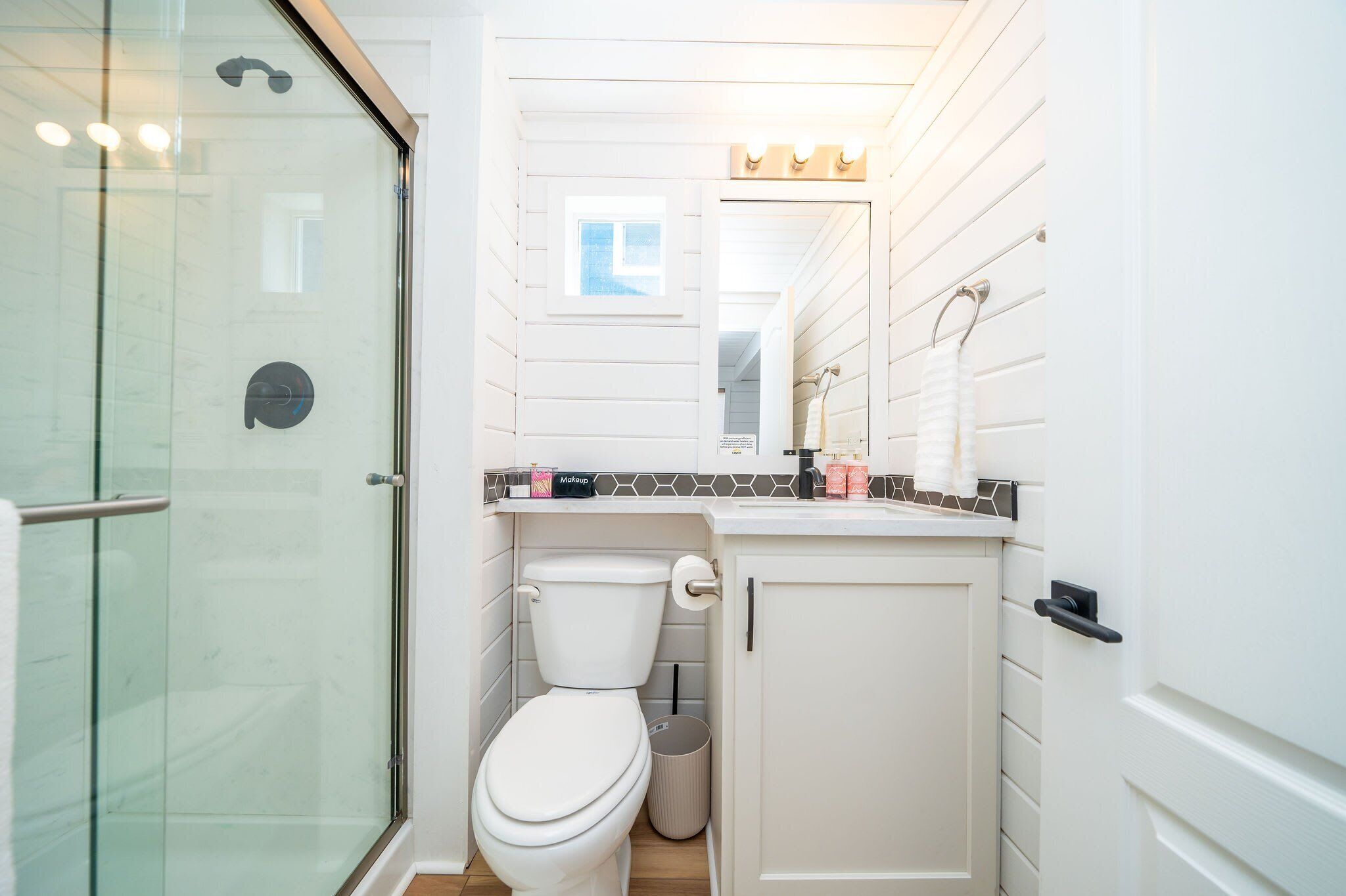 Un baño con cabina de ducha de vidrio, inodoro blanco y tocador con espejo y encimera.