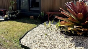 A modern building with a sliding glass door entrance, a small patio area with a table and chairs, and a garden with pebbles and plants. - Beach Serenity 1

Share

Save
 (Brighton-Le-Sands)