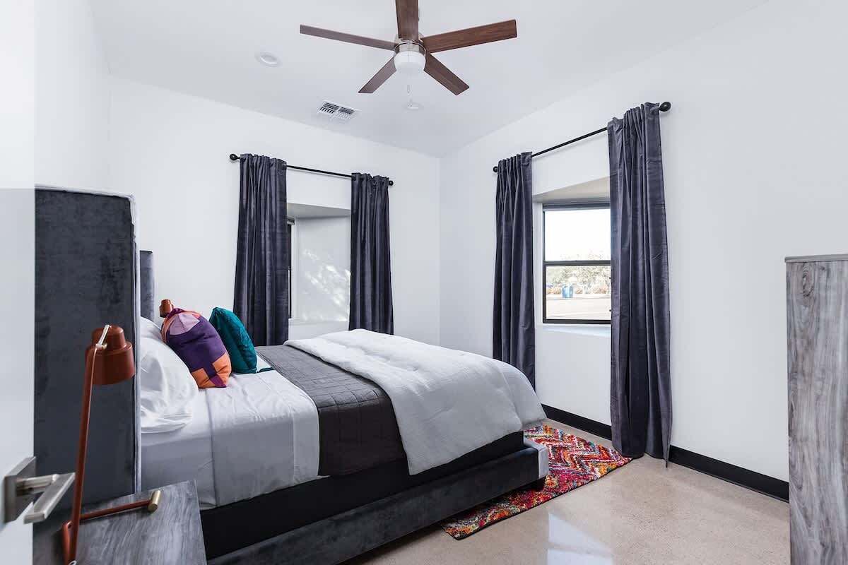 A modern bedroom with a bed, curtains, a ceiling fan, and a window.