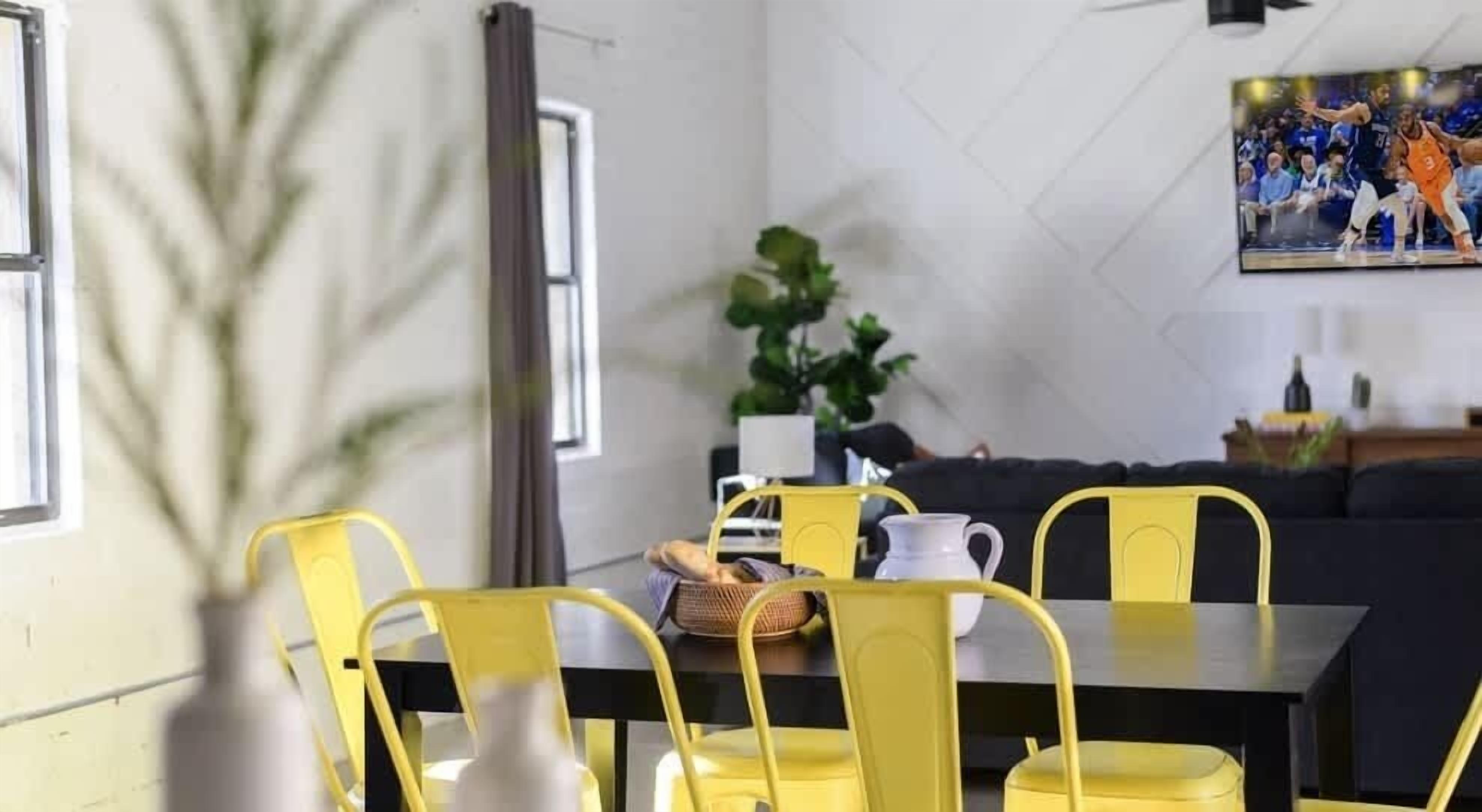 A dining area with yellow chairs, a black table, and a painting on the wall.