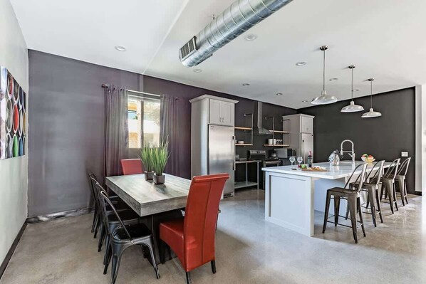 Cocina moderna con una isla central, comedor con sillas rojas y un ventanal con cortinas.