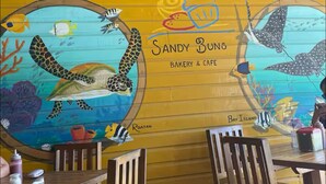 Interior de restaurante con un mural de una tortuga y peces, mesas de madera y luces colgantes.