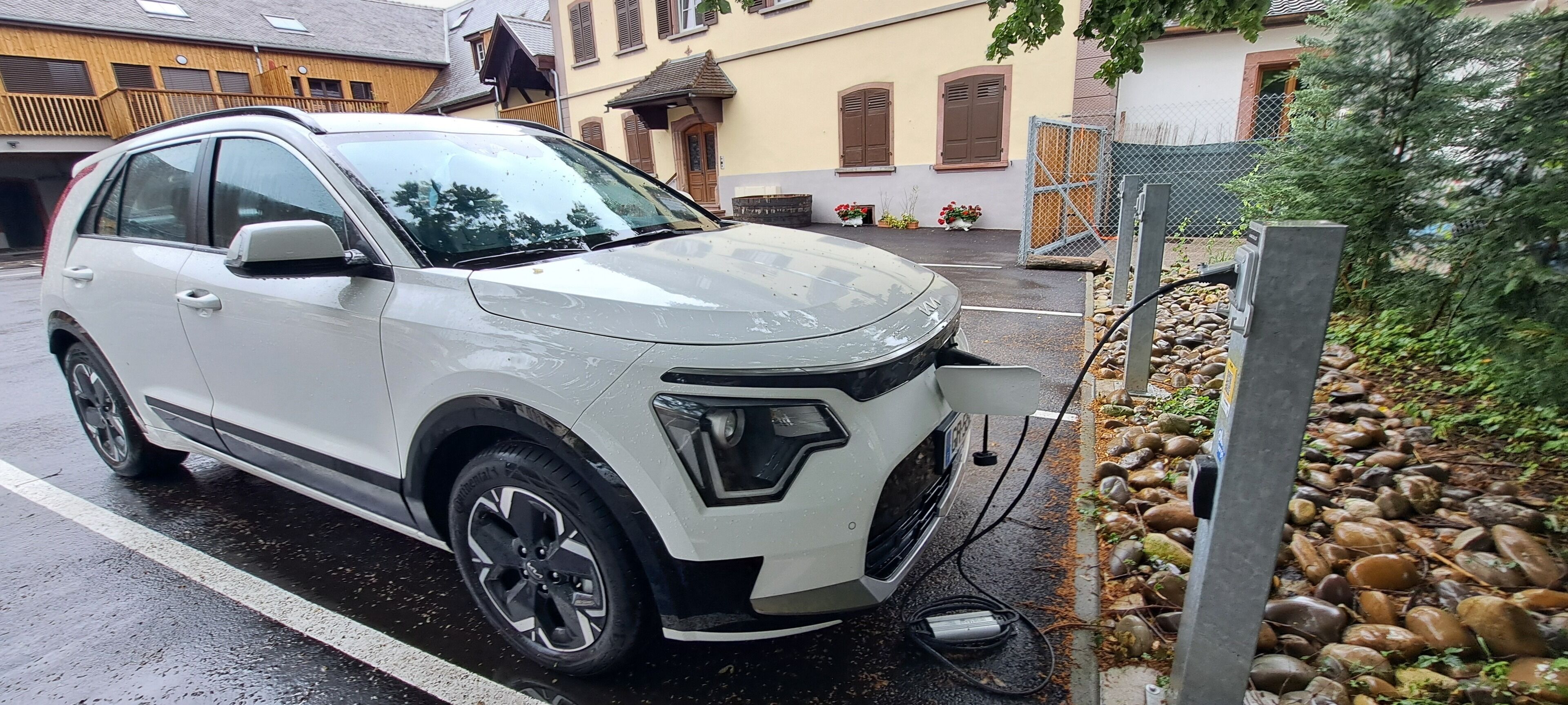 Een witte SUV geparkeerd op een natte straat, met een oplaadstation in de buurt.