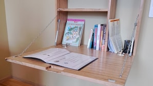 A wooden swing chair with a blue cushion, a wooden shelf with books and a small sign, and a wooden desk with a chair. - The Cozy Nest, Le Nid Douillet à Bergheim (Bergheim)