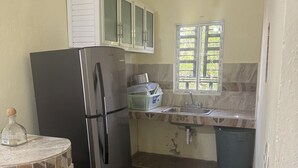Une cuisine avec un réfrigérateur noir, une fenêtre avec des stores, un évier et une poubelle.