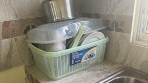 Une cuisine avec un évier en acier inoxydable, un égouttoir à vaisselle en plastique vert et une assiette blanche.