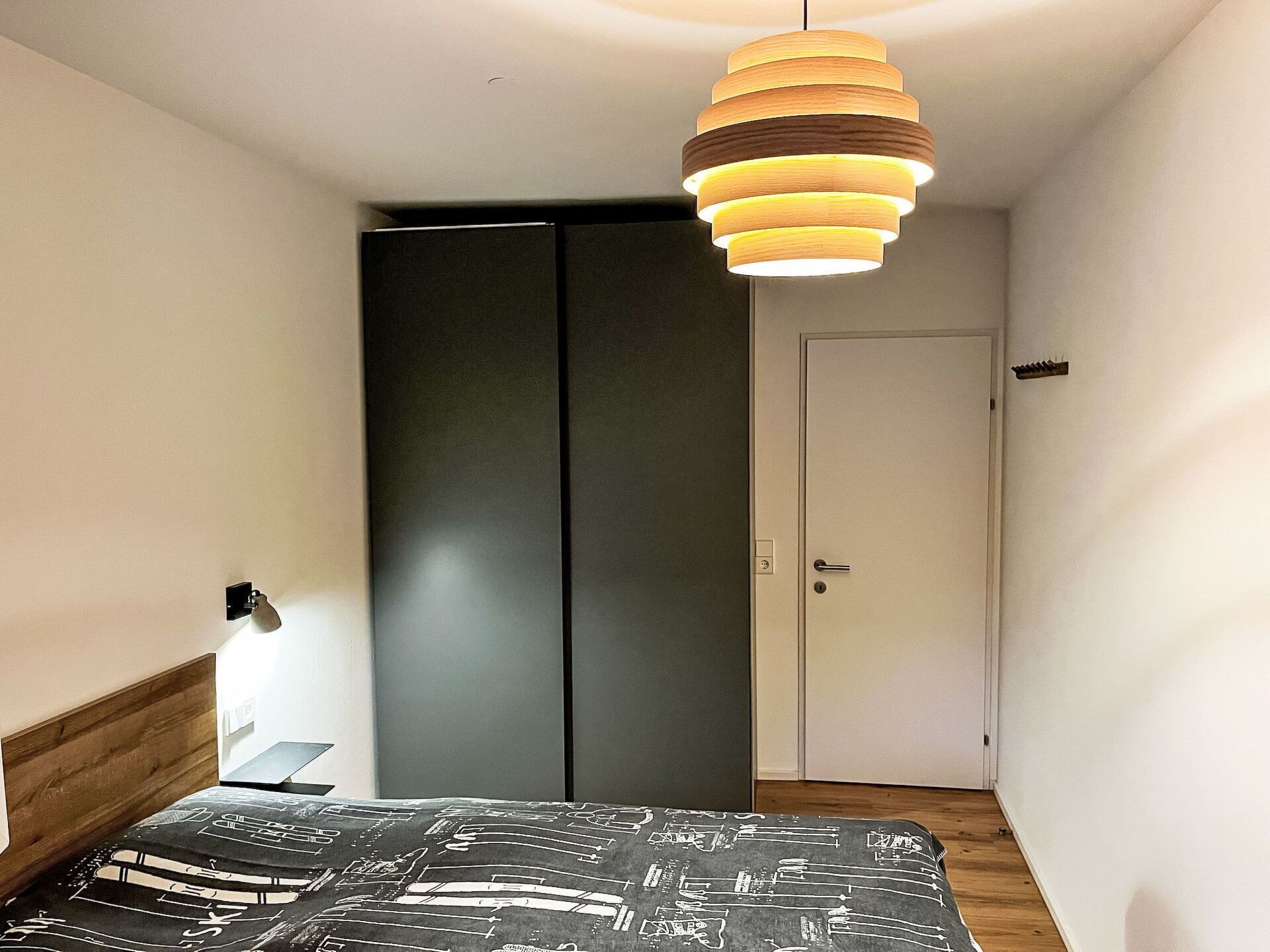 Un dormitorio con cama, armario, puerta y una lámpara colgante.