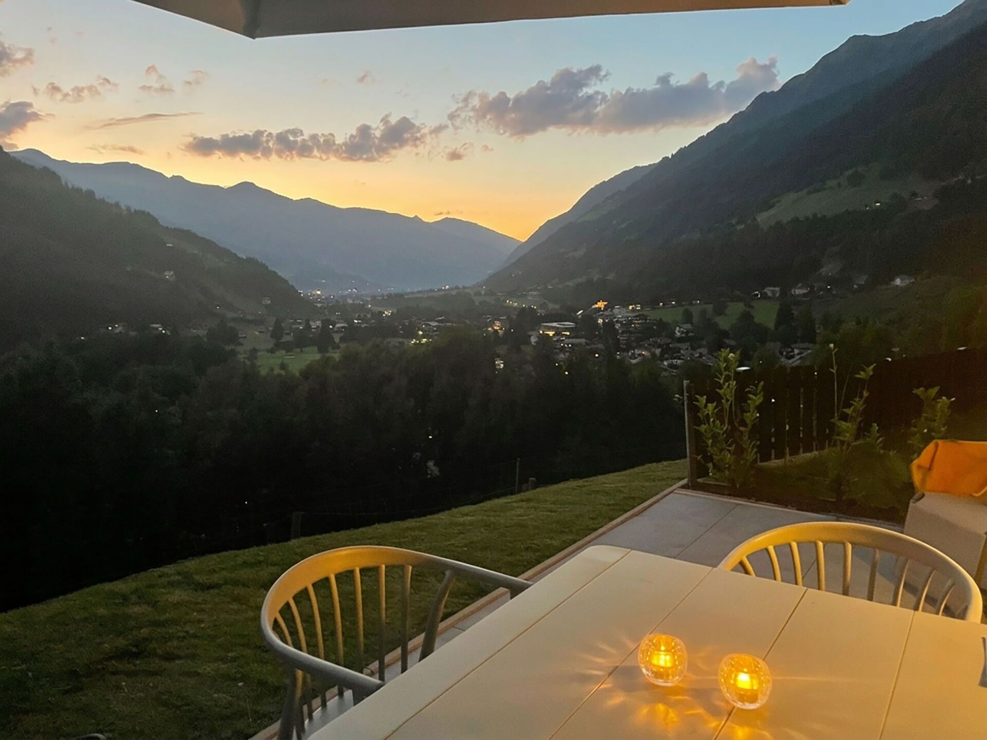 Una mesa con sillas y dos velas encendidas, con vista a un valle con montañas y un pueblo.