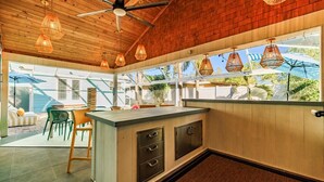 A kitchen with a wooden ceiling, hanging wicker lights, a bar counter, and a view of the outdoors. - Heated Pool~Hottub~Arcade~120"Screen~BBQ~Firepit (Bradenton)