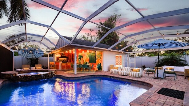 A covered outdoor pool area with a hot tub, lounge chairs, and umbrellas. - Heated Pool~Hottub~Arcade~120"Screen~BBQ~Firepit (Bradenton)