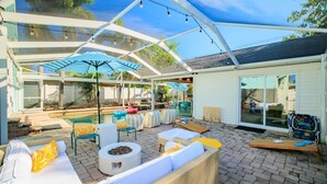 A covered patio with outdoor seating, a pool, and a glass-enclosed room. - Heated Pool~Hottub~Arcade~120"Screen~BBQ~Firepit (Bradenton)